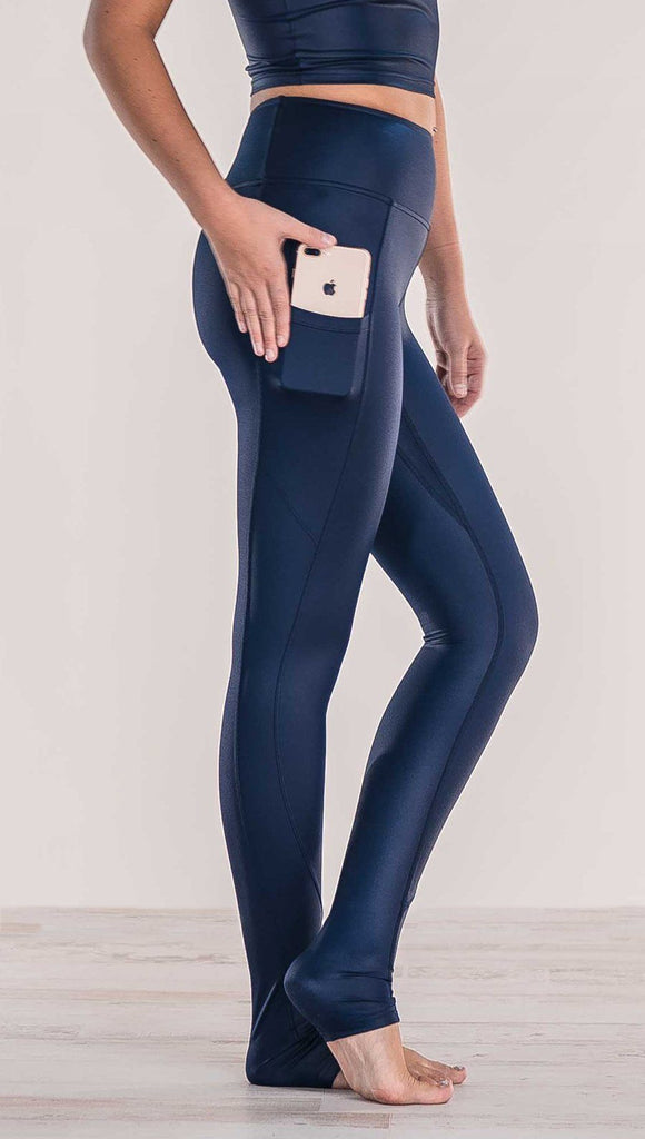 Close up side view of model wearing shiny midnight blue full length leggings putting iphone into right side pocket