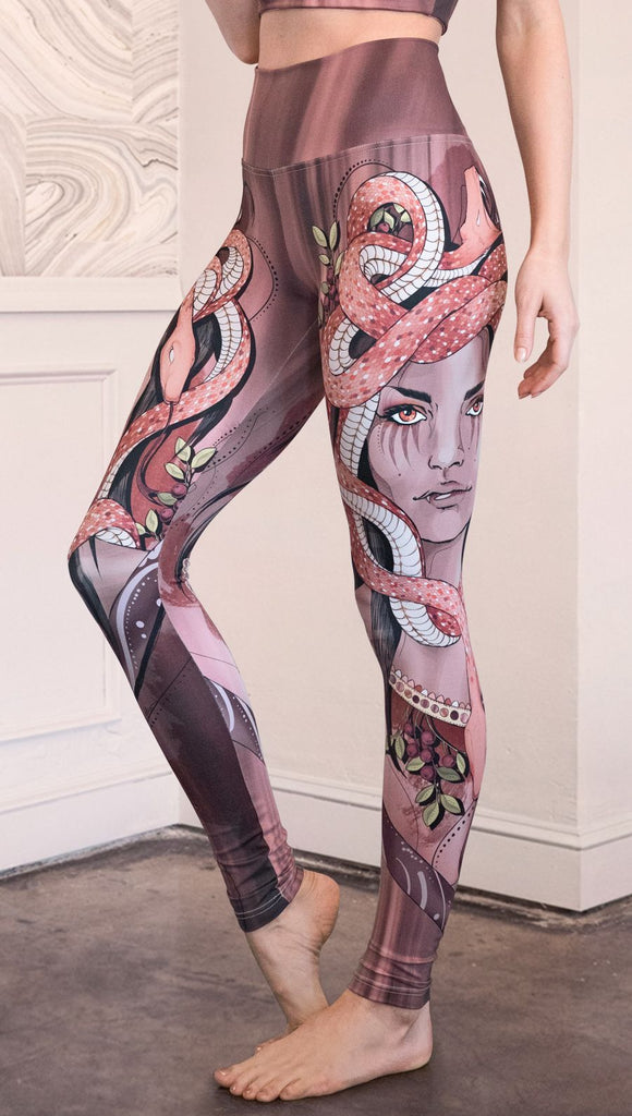 Left side view of the model wearing full length athleisure leggings with a mauve color medusa head and red, white, and black snakes