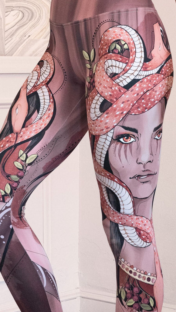 Zoomed in left side view of the model wearing full length athleisure leggings with a mauve color medusa head and red, white, and black snakes