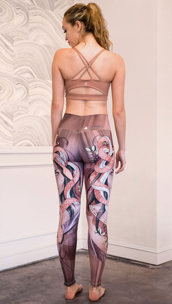 Back view of the model wearing full length athleisure leggings with a mauve color medusa head and red, white, and black snakes