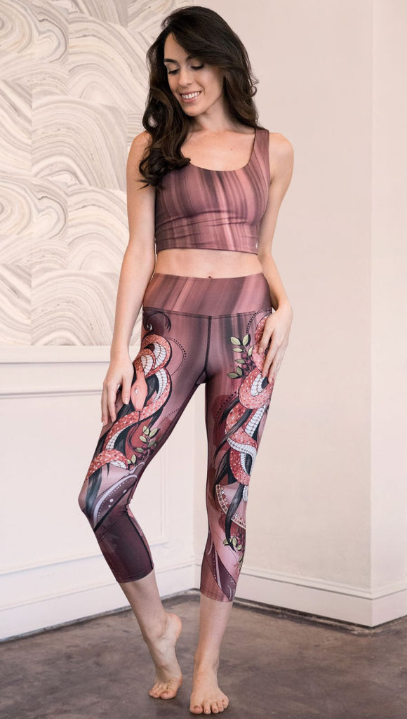Model wearing capri leggings with a mauve color medusa head and red, white, and black snakes