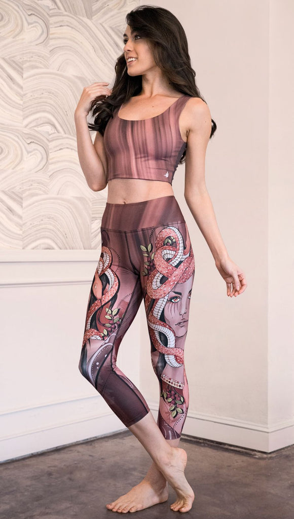 Zoomed out left view of model wearing capri leggings with a mauve color medusa head and red, white, and black snakes