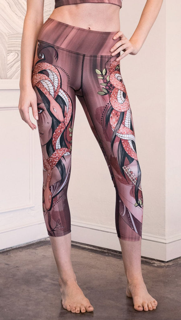 Zoomed in front view of model wearing capri leggings with a mauve color medusa head and red, white, and black snakes