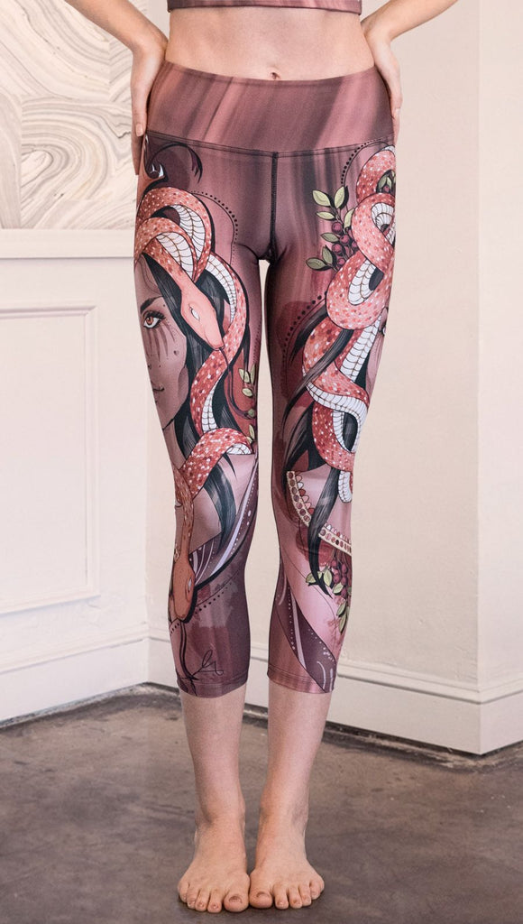 Front view of model wearing capri leggings with a mauve color medusa head and red, white, and black snakes