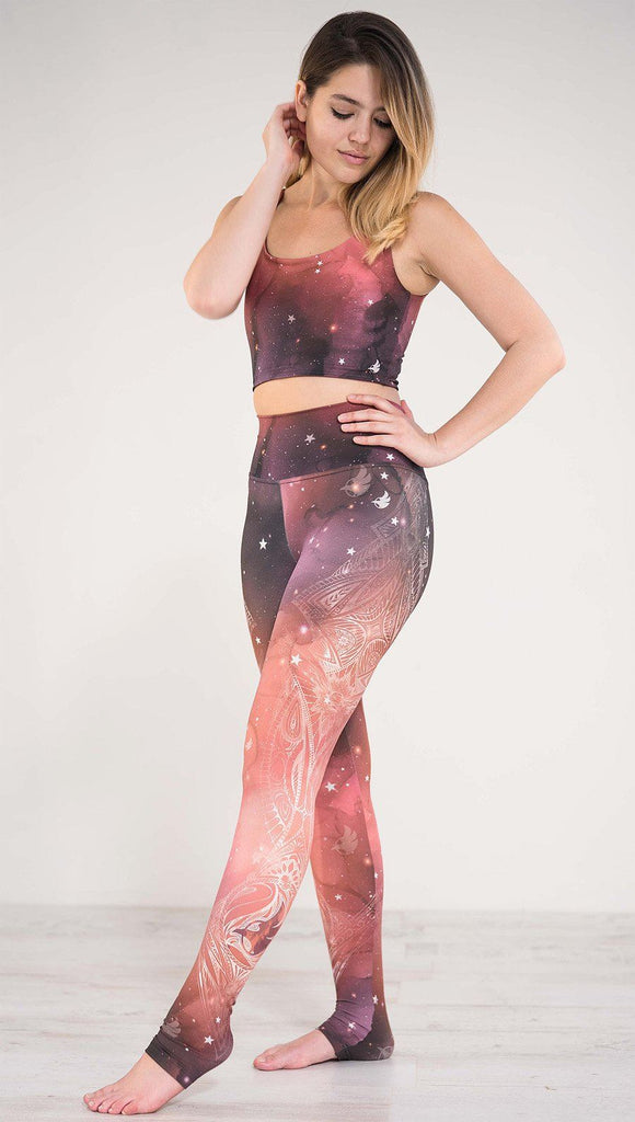 Model pointing toe wearing a red, orange and purple galaxy themed athleisure leggings with white henna inspired art running along the left side of the leg