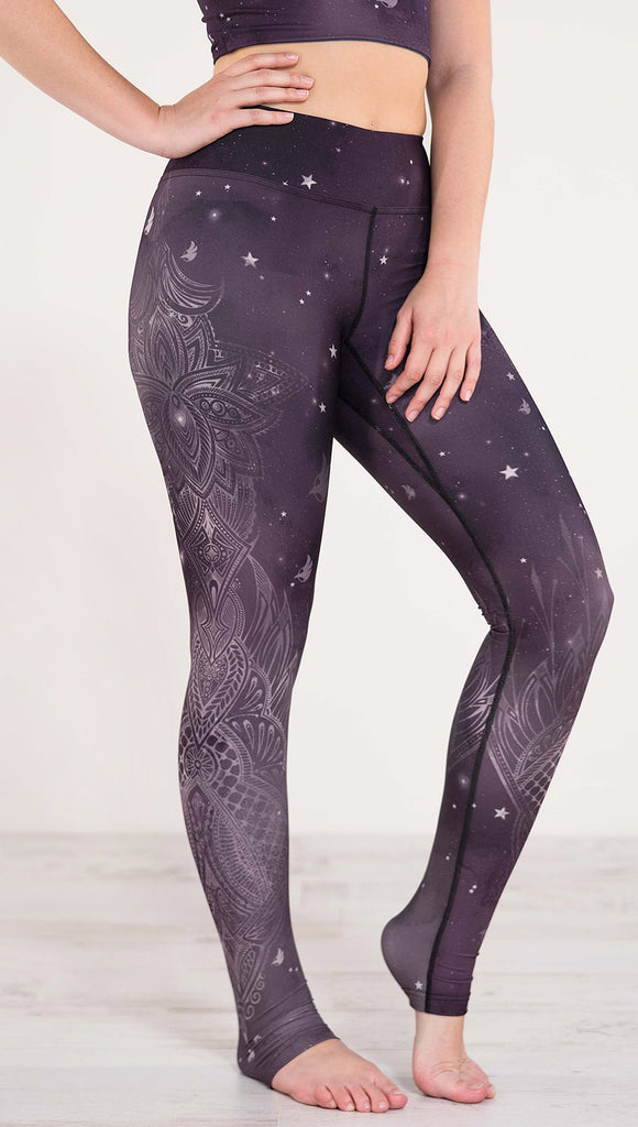 Right side view of model wearing purple galaxy themed triathlon leggings with white henna inspired flowers running along the right side of the leg