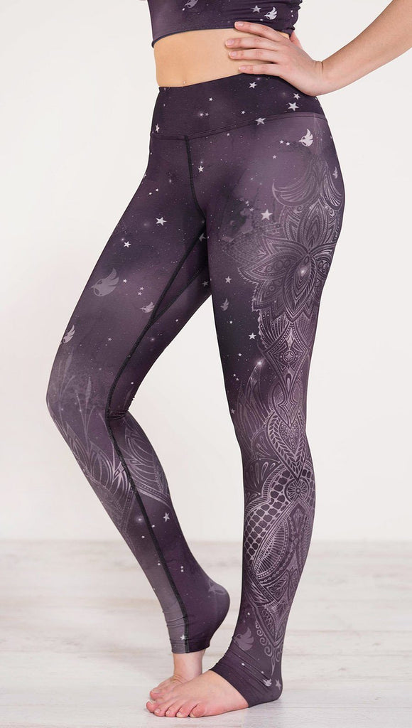 Left view of model wearing purple galaxy themed triathlon leggings with white henna inspired flowers running along the left side of the leg 