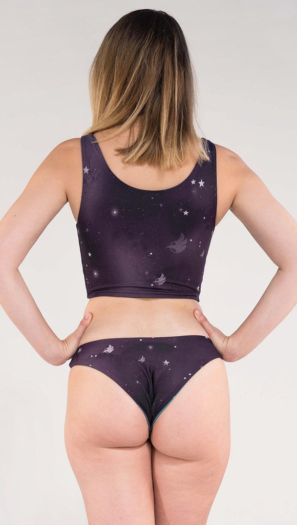 Back view of model wearing a purple galaxy themed low rise reversible bikini bottom called Galactic Moon Dust on this side