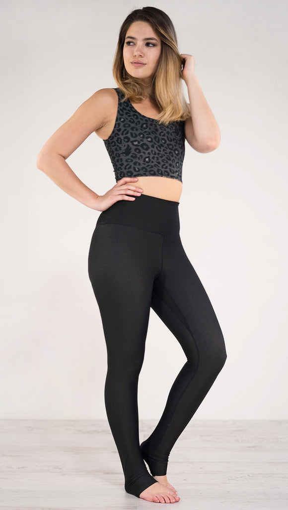Right side view of model wearing reversible charcoal leopard athleisure leggings in the reversed all black side showing