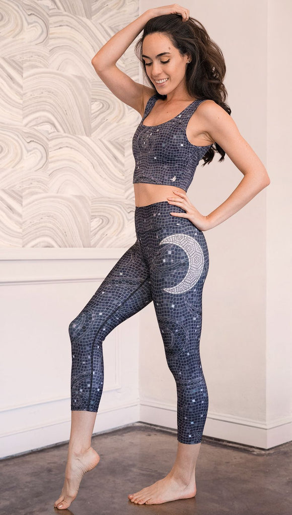 Left side view of model wearing mosaic printed capri leggings with moon artwork on left hip
