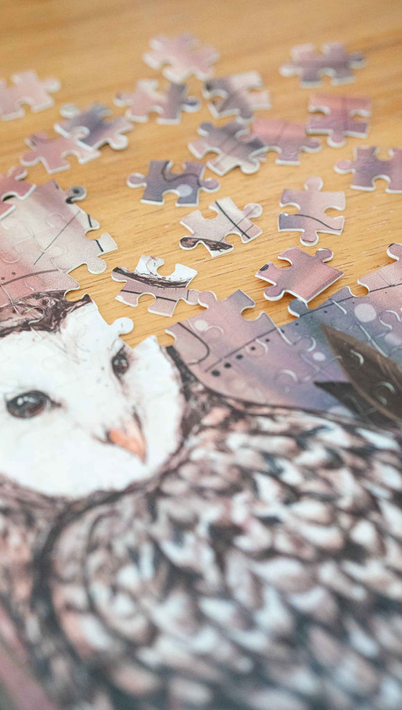 Partially disassembled WERKSHOP Barn Owl 252 piece jigsaw puzzle. The puzzle is printed with original artwork of an Owl by Chriztina Marie. It features a barn owl perched on top of a branch with whimsical leaves. The overall color story is of mauves, warm browns and complimentary green leaves. 