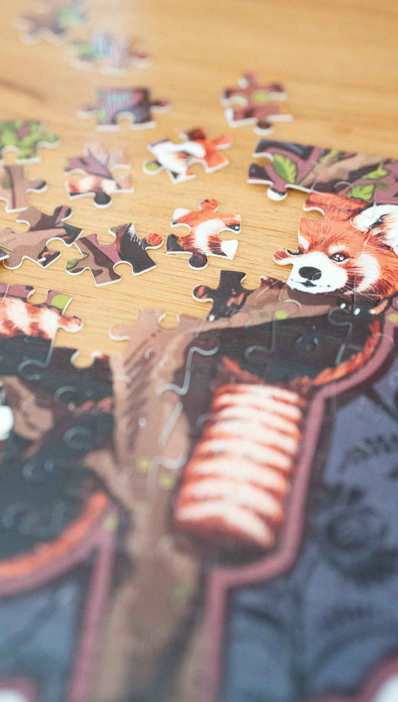 Partially disassembled WERKSHOP Red Pandas Puzzle. The artwork features 5 adorable red pandas playing near an abstract tree with a warm gray background.