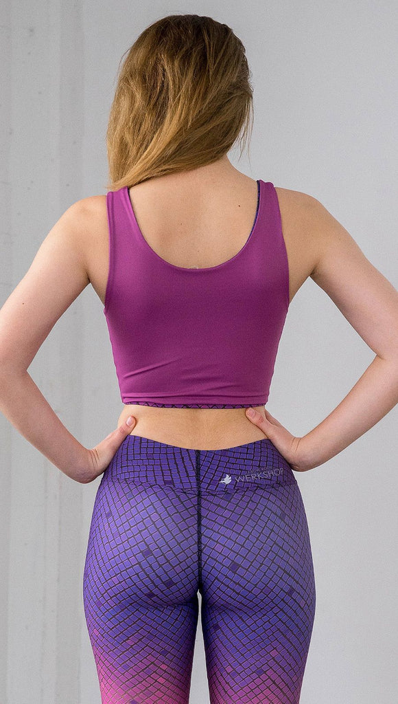 Three quarter length rear view of model wearing a fuschia reversible crop top with a purple mosaic tile print on the other side