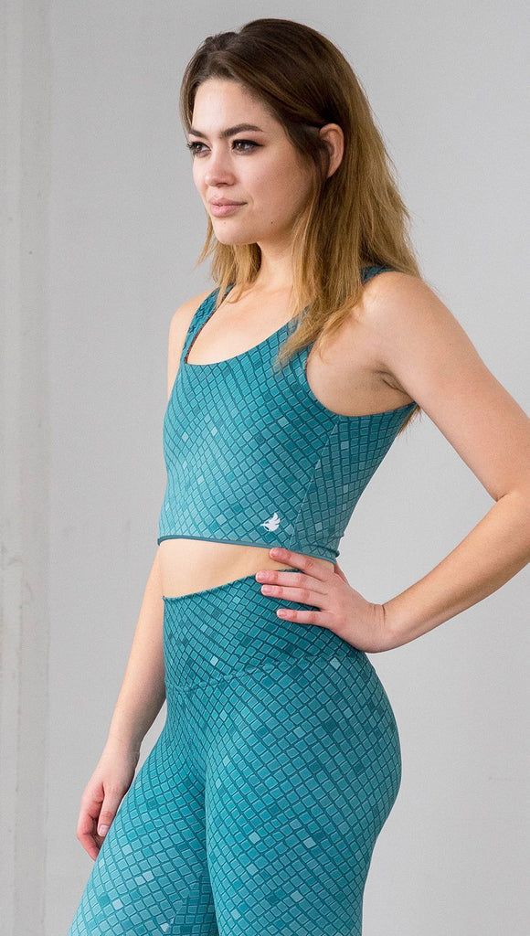 Three quarter length front left view of model wearing a teal mosaic tile print reversible crop top with solid teal on the other side