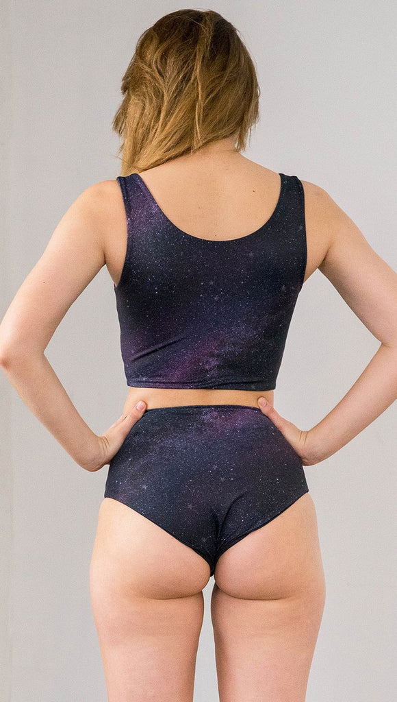 Closeup back view of model wearing reversible high-waist bikini bottom with celestial galaxy print on one side and black leather texture print on the opposite side