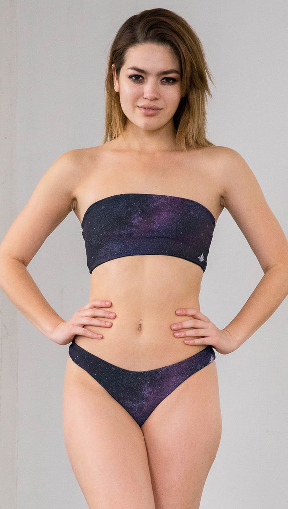 Closeup front view of model wearing reversible bikini bottom with celestial galaxy print on one side and black leather texture print on the opposite side