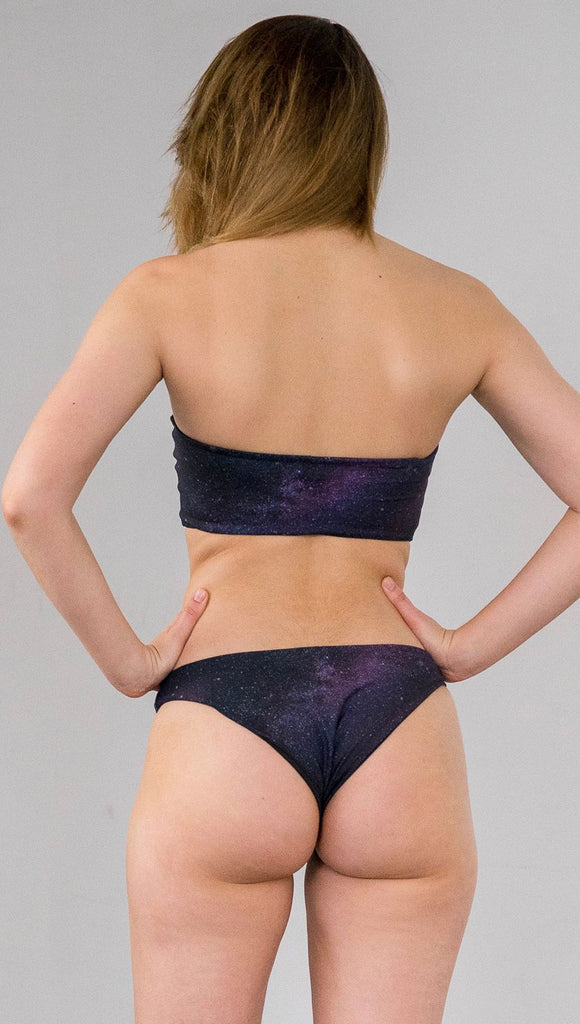 Closeup back view of model wearing reversible bikini bottom with celestial galaxy print on one side and black leather texture print on the opposite side