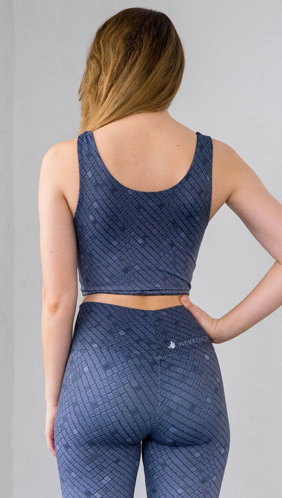 Three quarter length rear view of a model wearing a blue mosaic tile print reversible crop top with dark gray mosaic tile print on the other side 