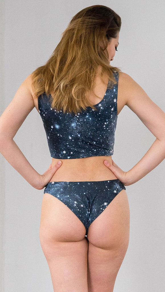 closeup back view of model wearing reversible bikini bottom with starry night galaxy celestial print on one side and black brushstrokes on the opposite side.