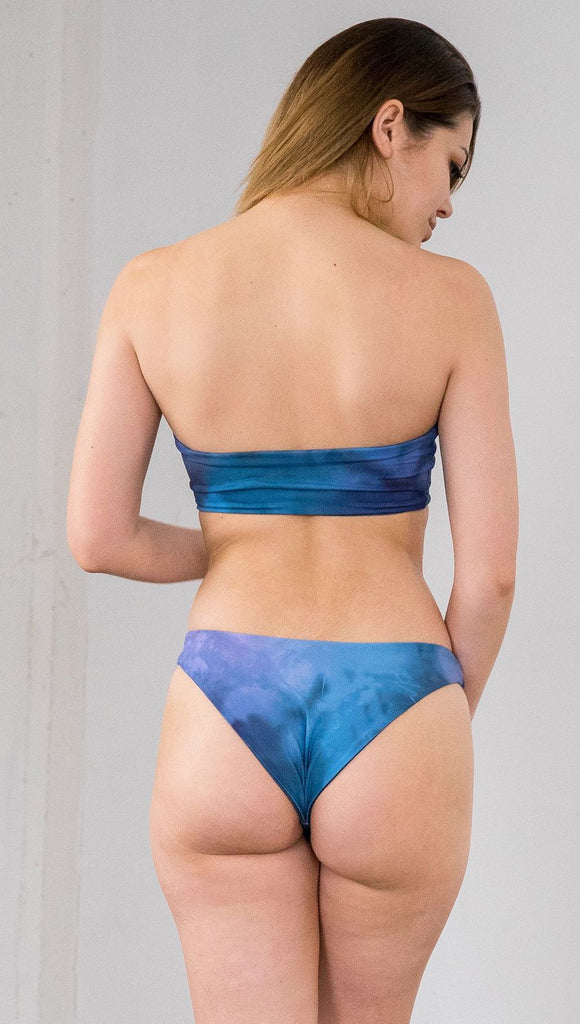 Closeup back view of model wearing reversible bikini bottom with ethereal dark blue water print on one side and textured watercolor print on the reverse side
