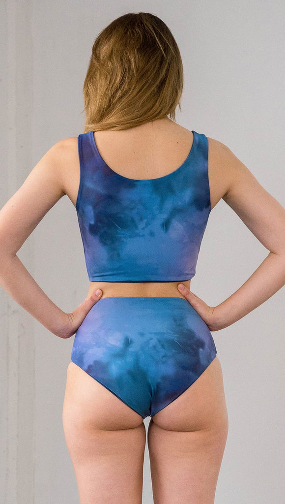 Closeup back view of model wearing reversible high waist bikini bottom with ethereal dark blue water print on one side and textured watercolor print on the reverse side
