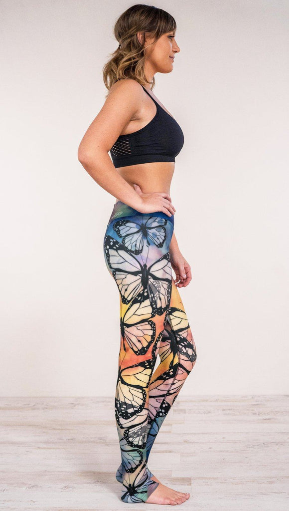Side view of model wearing WERKSHOP Full Length Triathlon Leggings with rainbow colors and monarch butterfly silhouettes 