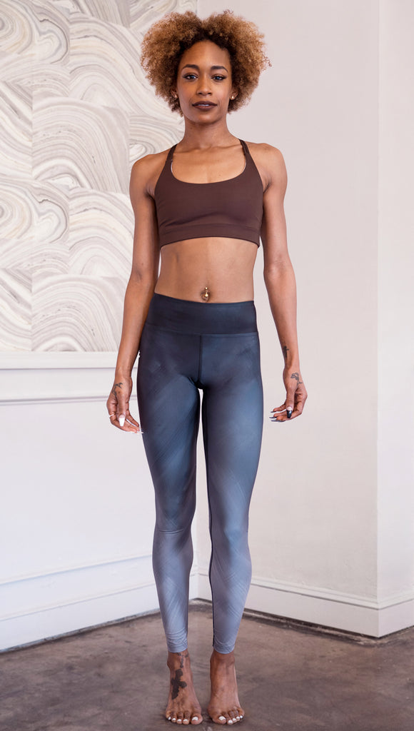Full body front view of model wearing WERKSHOP Black Rose Ombre leggings with a cluster of roses on the wearer's right calf (you cannot see the roses in this photo. the leggings look like a soft black ombre/fade from the front. darker on top and lighter on the bottom)
