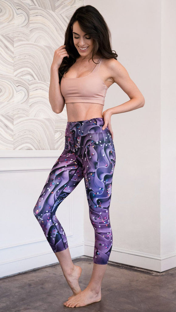 left side view of model wearing cupcake themed capri leggings with purple and royal blue frosting and rainbow colored sprinkle design