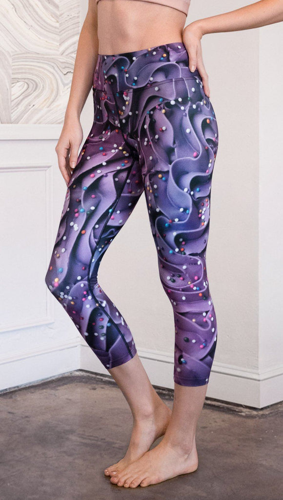 closeup left side view of model wearing cupcake themed capri leggings with purple and royal blue frosting and rainbow colored sprinkle design