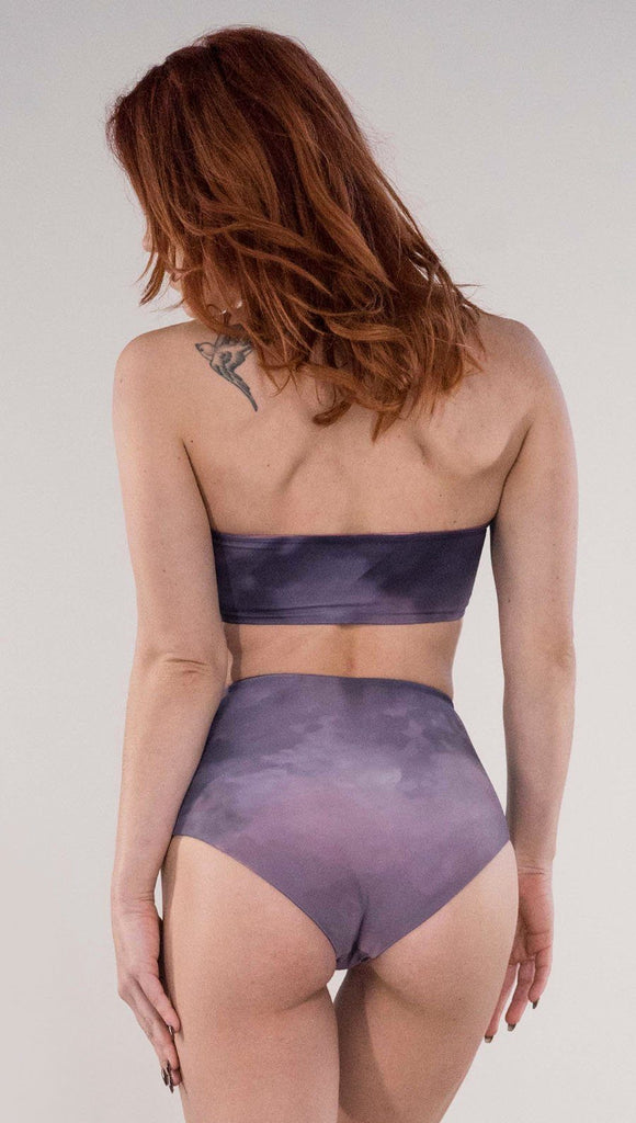 Back side view of model wearing the reversible Peacock high waist bikini bottom in the Peacock side in the colors purple and dark purple