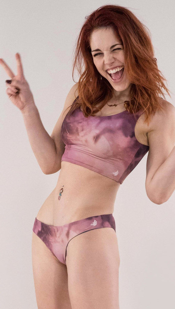 Left side view of model wearing the reversible Peacock low rise bikini bottom in the Rose quartz side in the colors pink and purple
