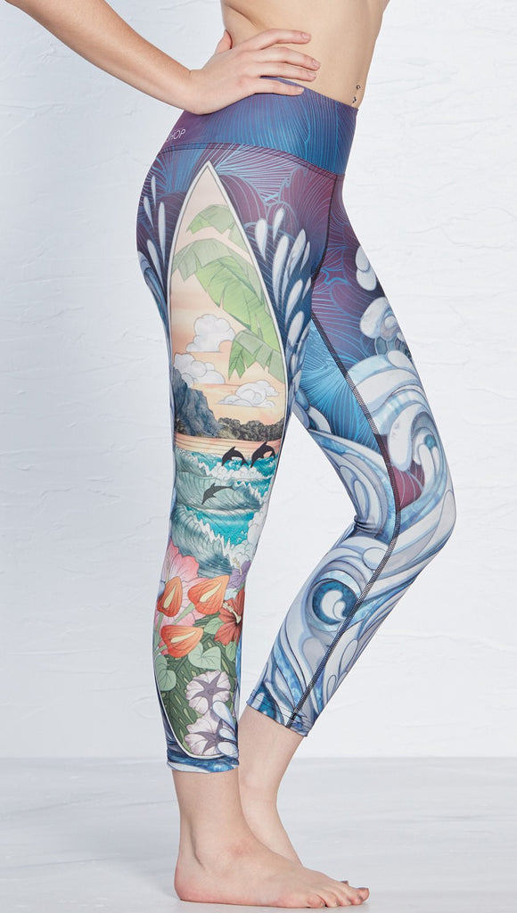 close up right side view of model wearing island surf board and waves themed printed capri leggings
