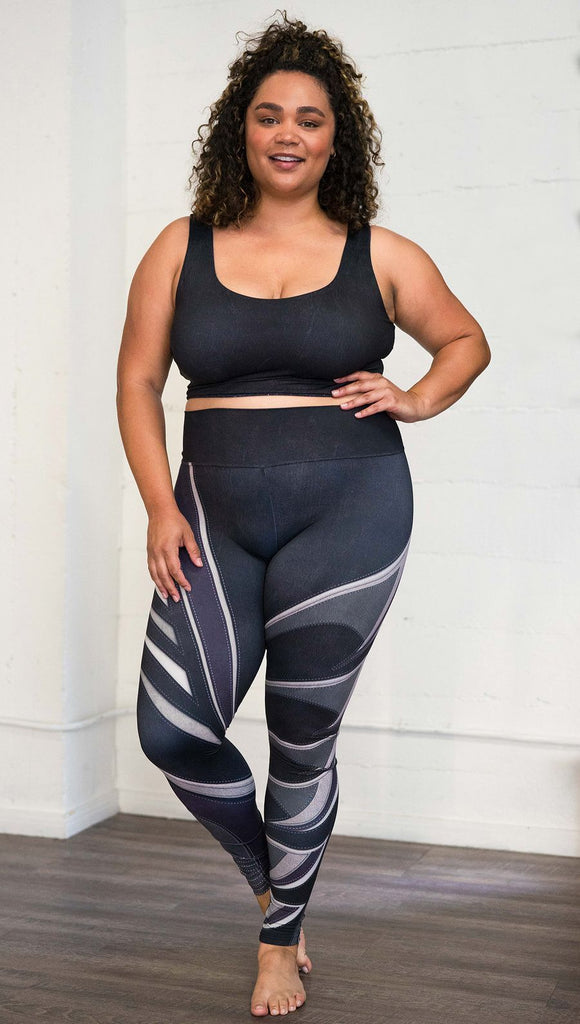 Front view of model wearing black printed full-length leggings with purple and gray stripe design