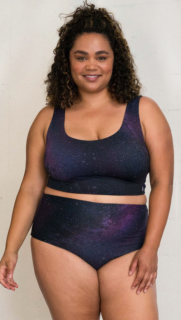 Closeup front view of model wearing reversible high-waist bikini bottom with celestial galaxy print on one side and black leather texture print on the opposite side