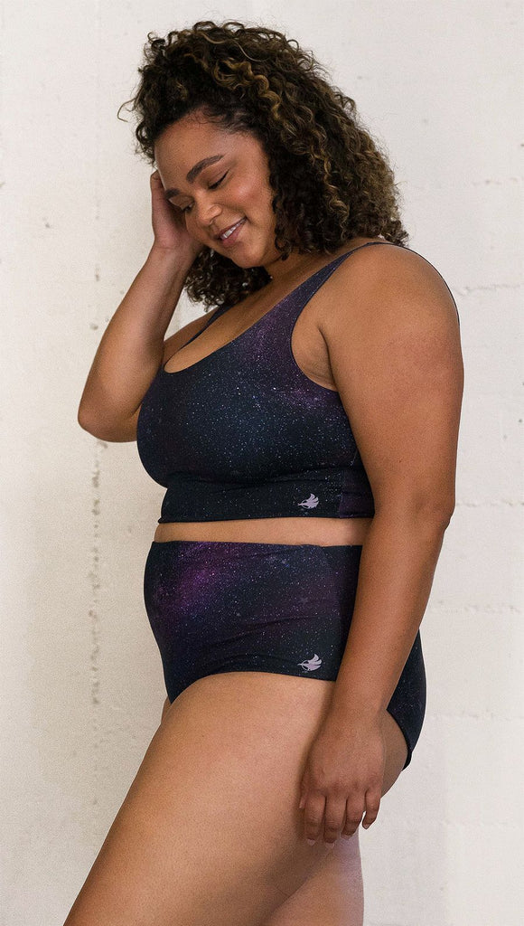 Closeup left view of model wearing reversible high-waist bikini bottom with celestial galaxy print on one side and black leather texture print on the opposite side