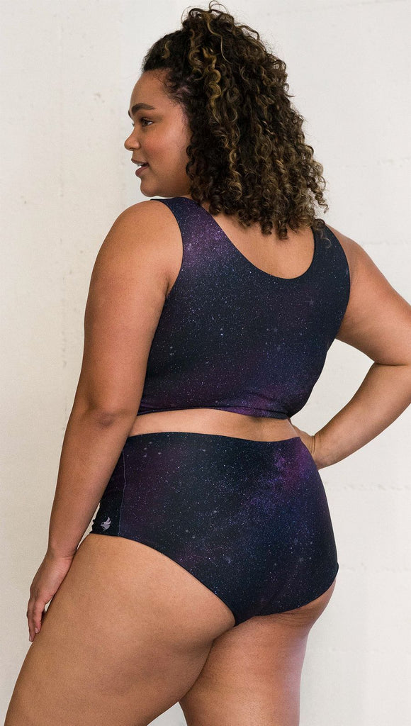 Closeup three quarter rear left view of model wearing reversible high-waist bikini bottom with celestial galaxy print on one side and black leather texture print on the opposite side