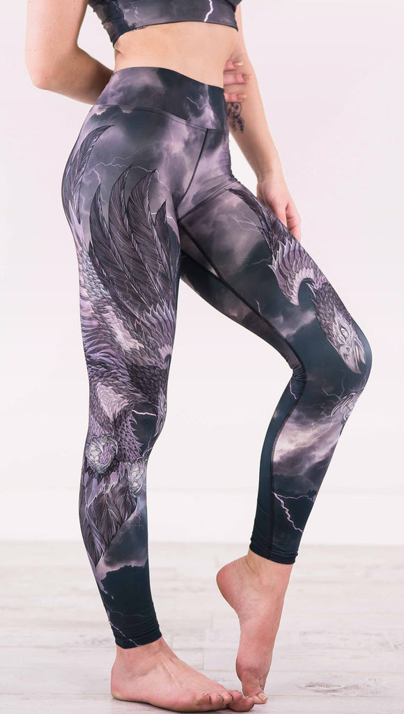 Right view of model wearing dark gray triathlon leggings with a large purple bird across the leg with lightning in the background