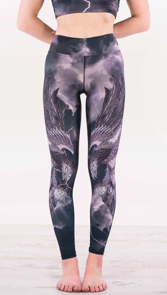 Enhanced front view of model wearing dark gray triathlon leggings with a large purple bird across each leg with lightning in the background