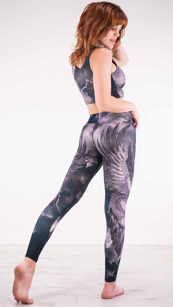 Back view of model wearing dark gray triathlon leggings with a large purple bird across each leg with lightning in the background