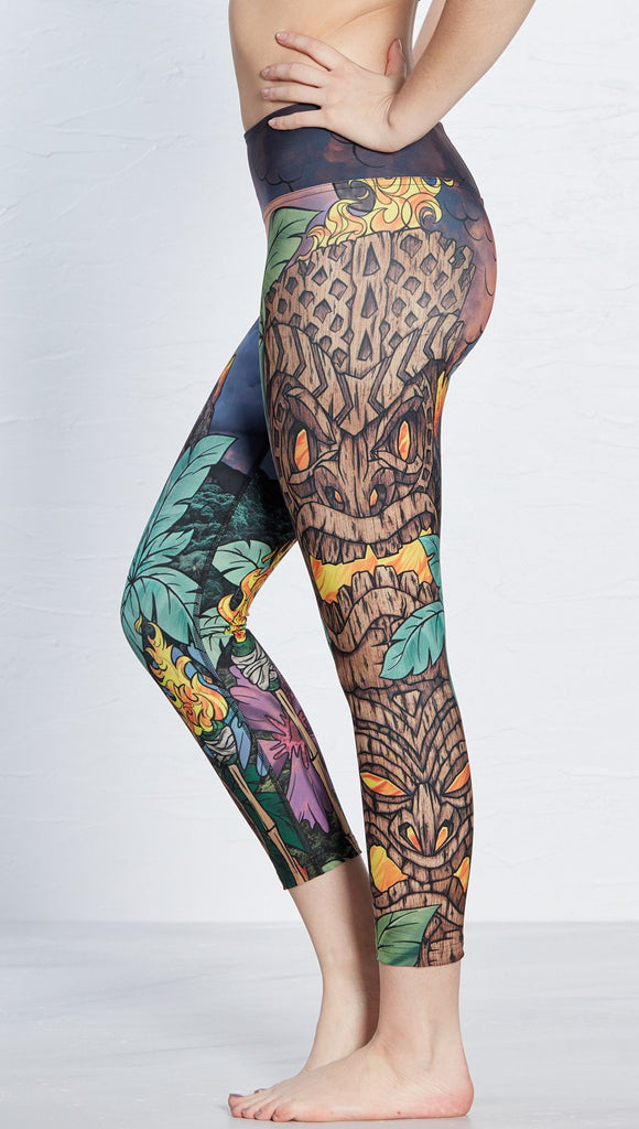 close up left side view of model wearing tiki torch themed printed capri leggings