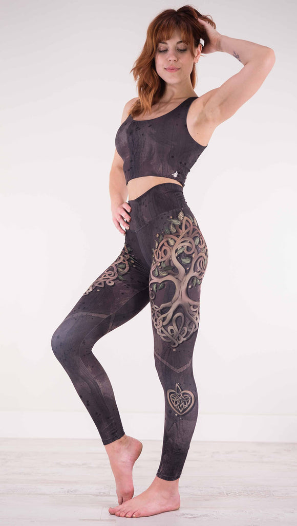 Left view of model wearing the Tree of Life athleisure leggings in a brown wood grain print with a tree across the side