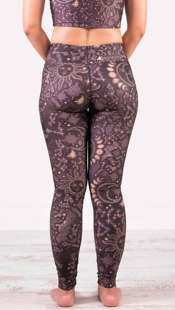 Back view of model wearing WERKSHOP Zodiac Full Length Triathlon Leggings. The zodiac themed artwork shows a hand-drawn sun and moon with the moon phases, shooting stars and all 12 zodiac constellations in gold over a dark purple background. Triathlon leggings do not have pockets.