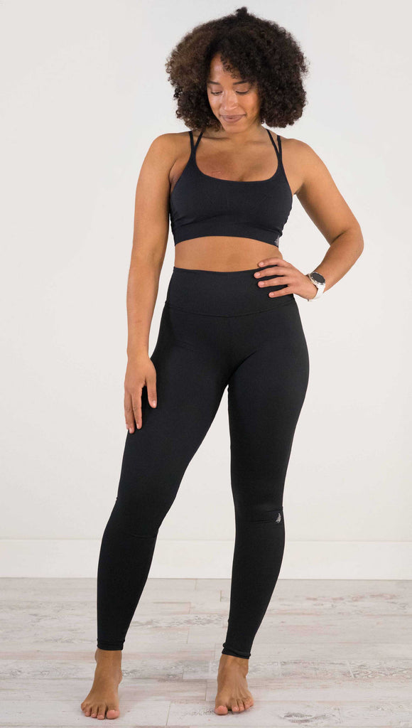 Full body front view of model wearing WERKSHOP Solid Black Athleisure Leggings with a small reflective eagle logo on the wearers left side calf