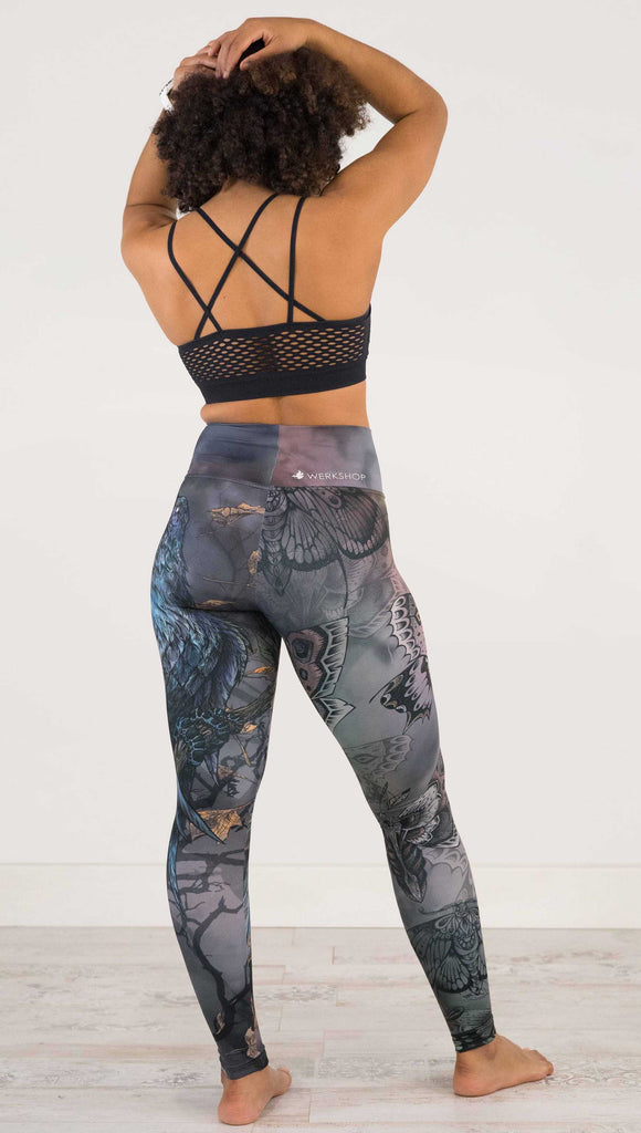 Full body back view of model wearing WERKSHOP Gothica Mashup Leggings. The leggings feature original artwork with moths over a muted/dark oil-slick inspired background on one leg and a spooky scene with a raven and a moon on the other leg.