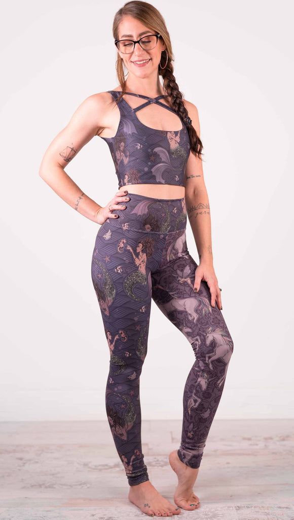 Model wearing WERKSHOP Mermaid and Unicorn Mashup Athleisure Leggings. The leggings feature mermaid artwork on the wearers right leg with a dark blue background and unicorns over a purple background on the wearer's left leg.