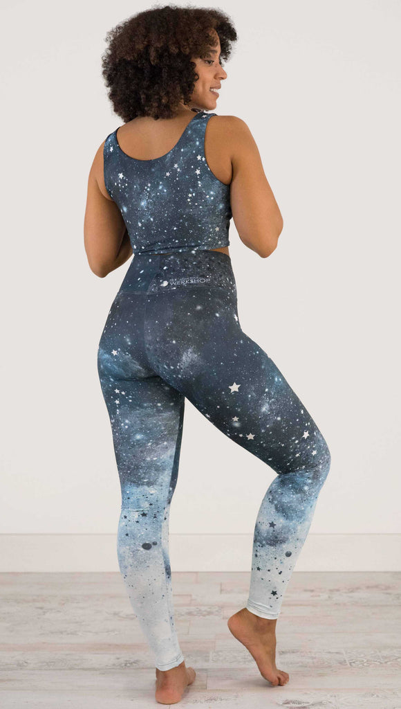 full body back view of a girl wearing our moon phases athleisure leggings - with the phases of the moon printed on the wearer's left leg on a starry night sky with all zodiac constellations in the background