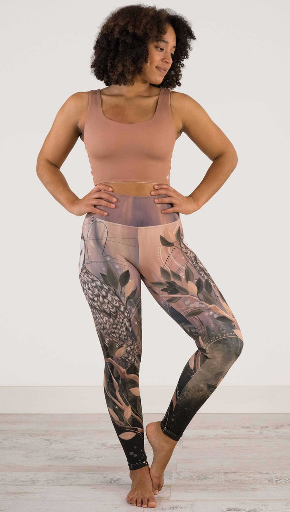 Full body front view of model wearing WERKSHOP Owls Athleisure Leggings. The leggings are printed with a whimsical barn owl on the thigh surrounded by swirls and leaves on a mauve and cream toned background.
