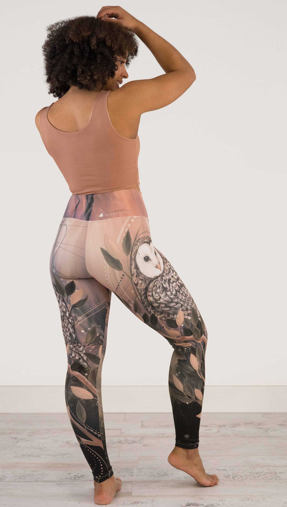 Full body back view of model wearing WERKSHOP Owls Athleisure Leggings. The leggings are printed with a whimsical barn owl on the thigh surrounded by swirls and leaves on a mauve and cream toned background.