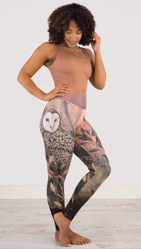 Full body side view of model wearing WERKSHOP Owls Athleisure Leggings. The leggings are printed with a whimsical barn owl on the thigh surrounded by swirls and leaves on a mauve and cream toned background.