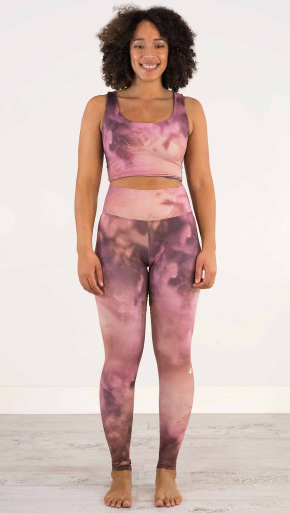 Full body front view of model wearing WERKSHOP Rose Quartz Athleisure Leggings. The leggings are printed with a warm rose/mauve and peachy watercolor effect with our eagle logo printed on the wearers outside left calf.